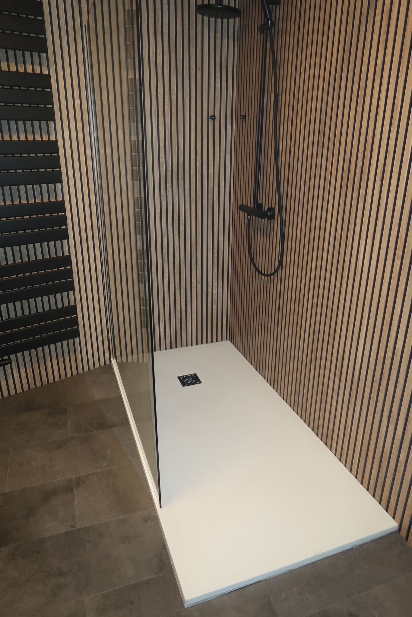 Stijlvolle inloopdouche met houtlook wandbekleding, zwarte regendouche en donkere vloertegels.